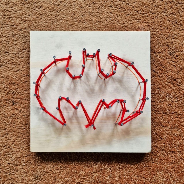 Dit spijkerplankje maak je met een stukje hout, spijkers en wat wol. Eerst teken je de vorm op het plankje. Sla vervolgens de spijkers er in en draai de wol daar omheen. Onze jongen van 12 jaar maakte het Batman logo.