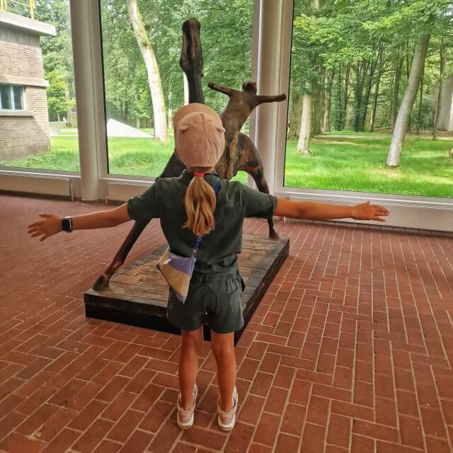 Kröller-Müller Museum en Nationaal Park de Hoge Veluwe met kinderen. Het museum ligt echt midden in de natuur en het bos komt overal naar binnen. Het is daardoor ook een museum met veel daglicht. En nee, kleine meis deed niet zo maar wat bij dit kunstwerk van Mario Marini, dit was een opdracht tijdens het speurspel! Daarover hieronder meer.