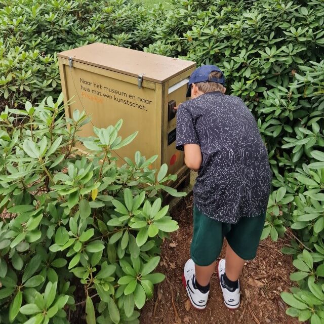 Kröller-Müller Museum en Nationaal Park de Hoge Veluwe met kinderen. Heel leuk voor wat oudere kinderen en tieners: Kröller-Müller Museum heeft een eigen geocaching route. Echt wat voor onze jongen, die is gek op digitaal speuren. Je kiest een route langs 5 of 11 kunstwerken, wij gingen voor de lange route. Al speurend loop je dus dwars door de beeldentuin. Bij ieder kunstwerk dat je vindt, moet je een vraag beantwoorden en krijg je meer informatie als je op de i klikt. Zoals hier bij het kunstwerk Green Room van Marien Schouten. Uiteindelijk ga je op zoek naar een kunstschat en krijg je een kleine beloning in de museumwinkel.