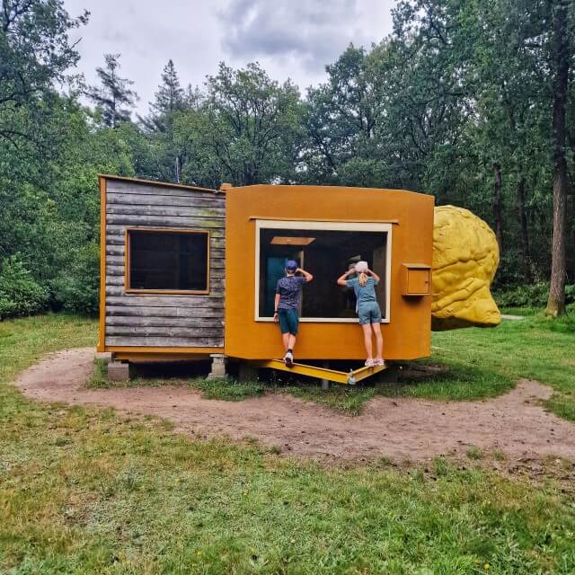 Kröller-Müller Museum en Nationaal Park de Hoge Veluwe met kinderen. Juist omdat het zo groot is hebben kinderen de ruimte om lekker rond te rennen. In iedere uithoek kom je weer nieuwe kunstwerken tegen. Voor sommige moet je zelfs omhoog klimmen over een pad. Of kun je naar binnen turen, zoals dit fascinerende mobiel huis van Joep van Lieshout. 